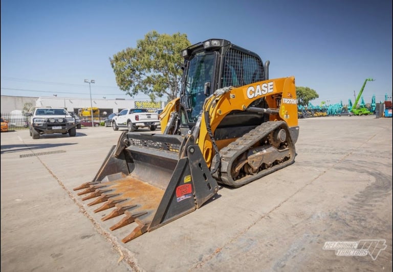 Yellow and black compact track loader with bucket attachment parked in industrial lot under clear sky