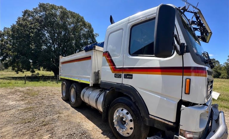 White and red dump truck with cargo bed parked in field with trees and clear blue sky