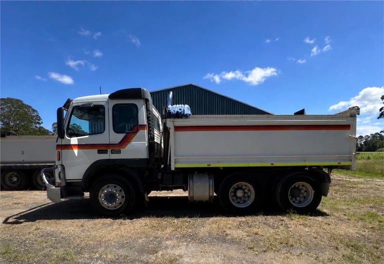 White and red industrial dump truck with tipper bed parked on gravel against blue sky